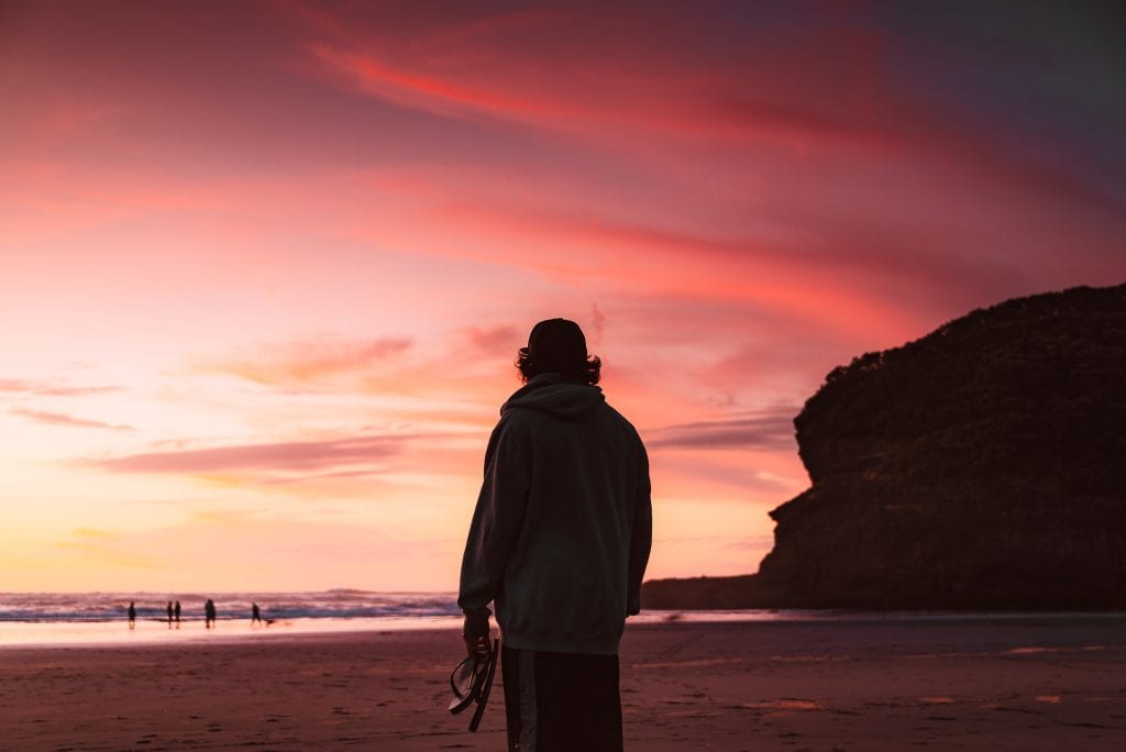 a man watching the sunset at bethells beach te henga