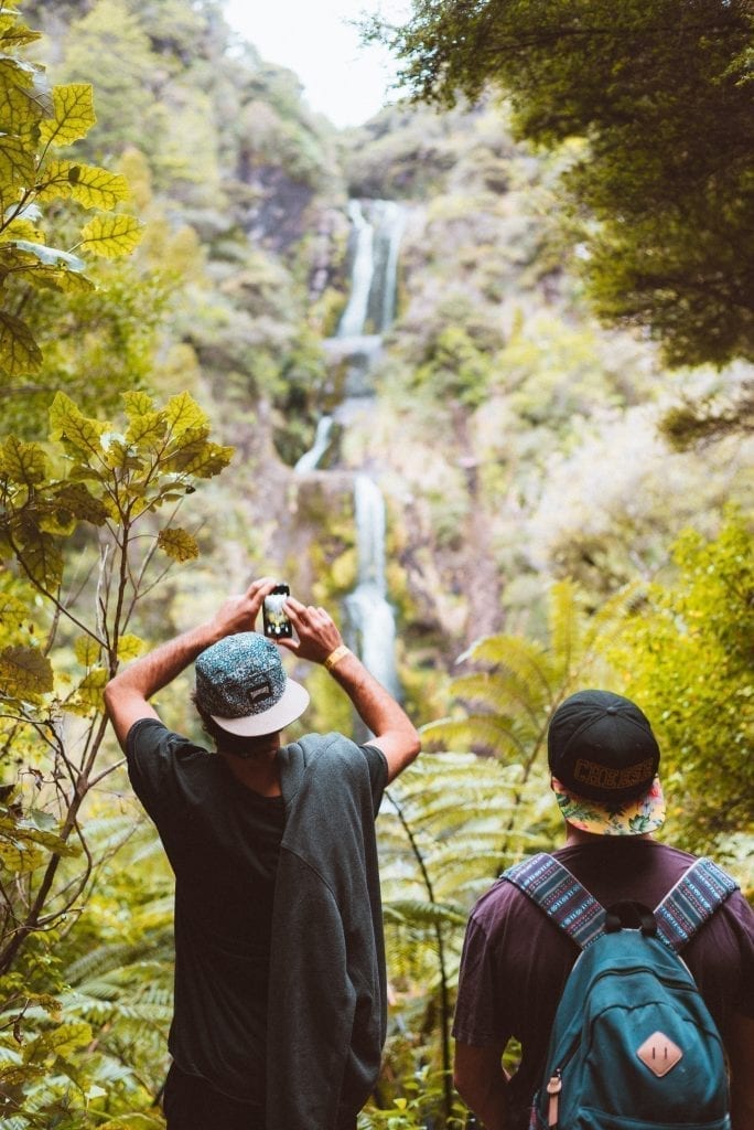 friends taking pictures of kitekite falls at piha