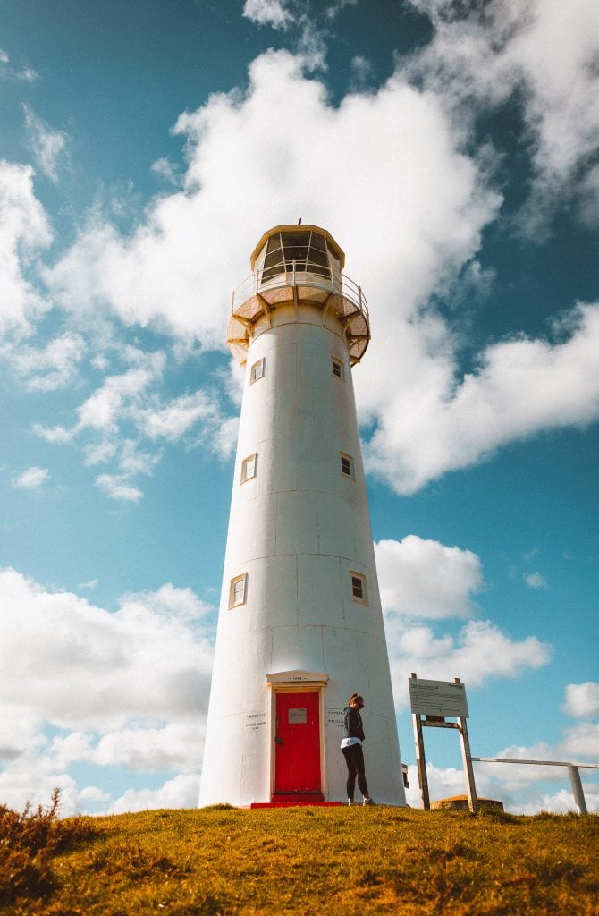 a lady standing in front of cape egmont lighthouse in taranaki