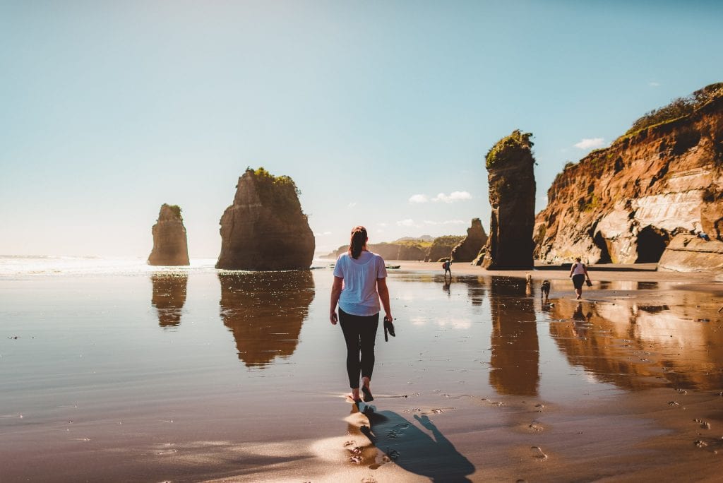a woman walks towards the three sisters at tongaporutu in taranaki